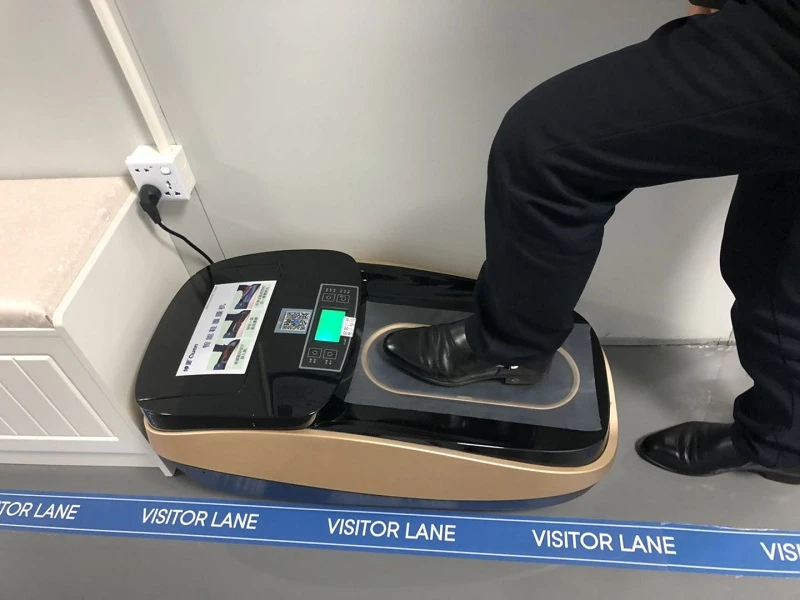 Visitor using QUEN shoe cover dispenser at a factory entry