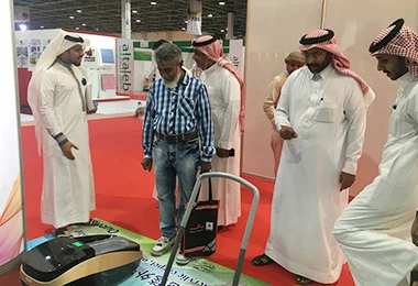 Visitors testing QUEN shoe cover machine at a Middle East trade show